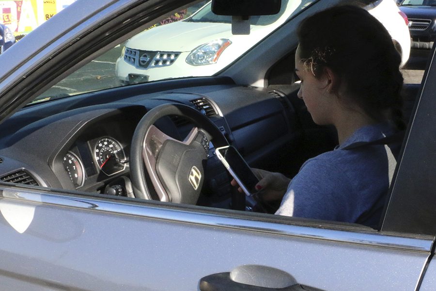 Junior Morgan McEntire looks at her phone before leaving the junior lot. While this is OK while parked, “beginning drivers definitely need to keep their phones off and put away,” Mr. Greg Bamrick, school counselor and driver education instructor said. 