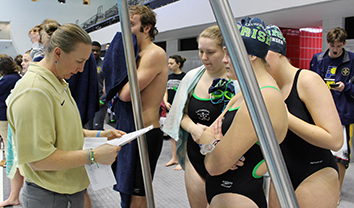 Coach Ms. Ashley Hill discusses events with seniors Lizzy Jensen, Bailey Snyder and Hannah Tuttle on Senior Night during the meet against Roncalli.