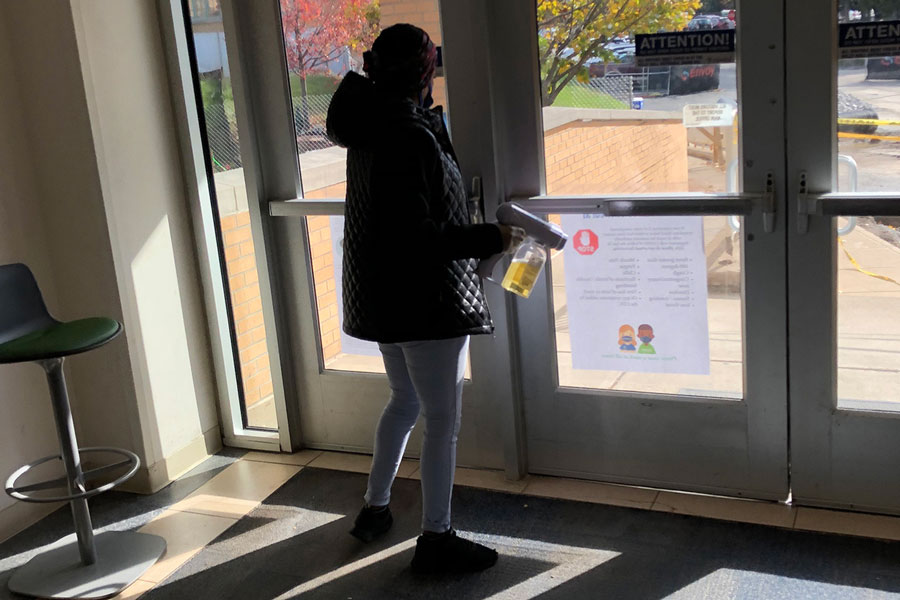 Immediately after a passing period on Oct. 29, an EMS staff member disinfects the door handles on the southwest entrance of Kelly Hall. 