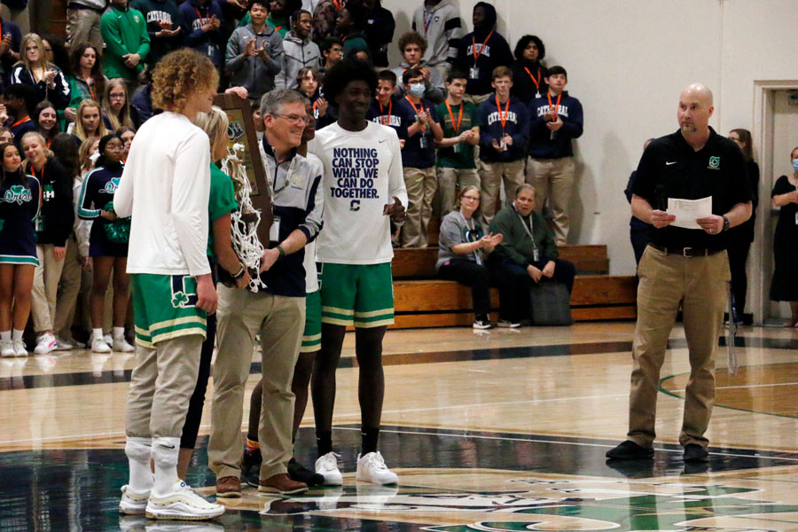 As Head Coach Mr. Jason Delaney looks on, members of the mens basketball team present the Class 4A State championship trophy to the school. 