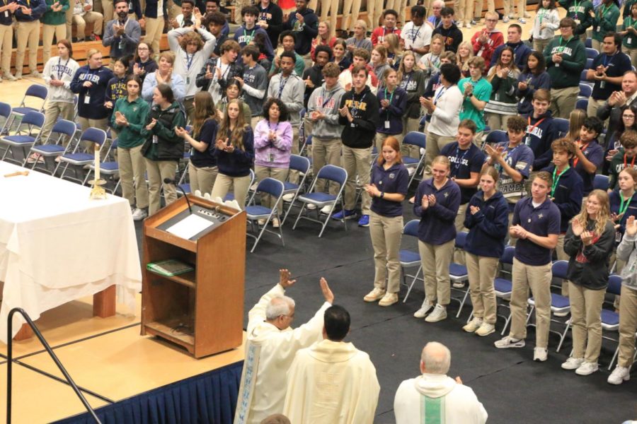 Many students enjoy sitting on the floor, while the remainder of the student body and staff sit in the bleachers to celebrate the Mass.