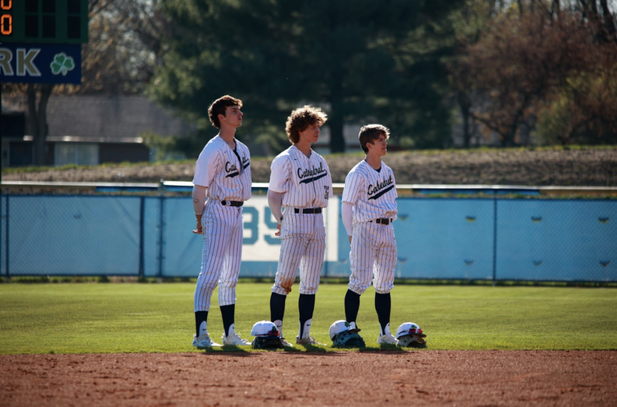Caption: Seniors David Ayers and Kyuss Gargett and freshman Eli Sinsabaugh (L-R) pause for the national anthem before a game versus Zionsville on April 11. The Irish beat the Eagles 5-4. 