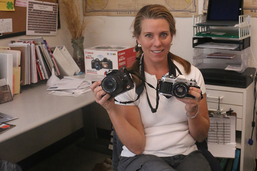 Photography teacher Ms. Joellen Desautels poses in her classroom, Cunningham 1220, with the types of cameras for which she seeks donations.