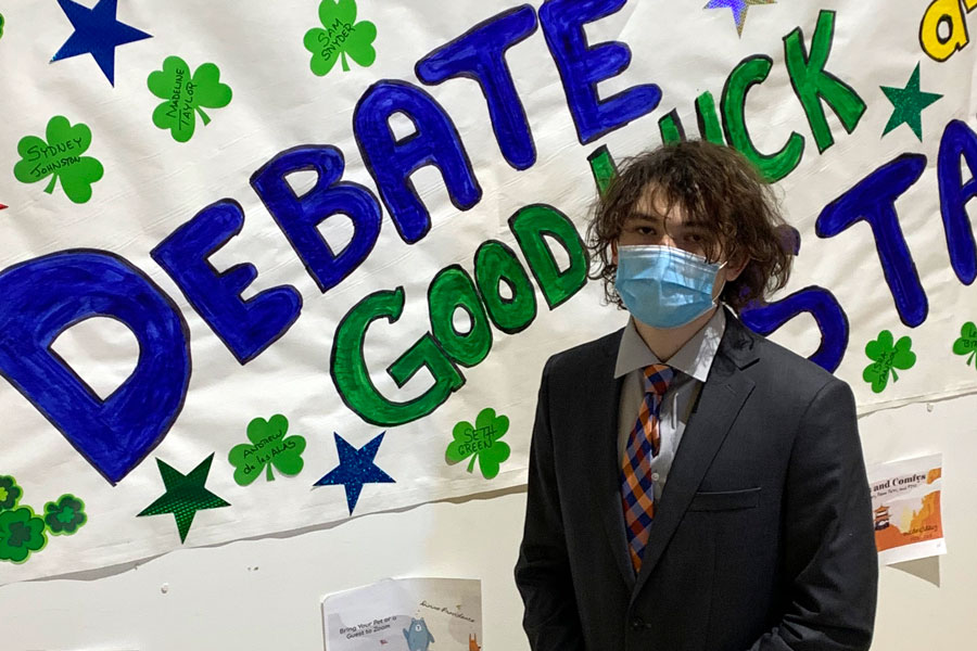 Junior Lendon Bryam stands in front of the speech and debate sign in Kelly Hall. 