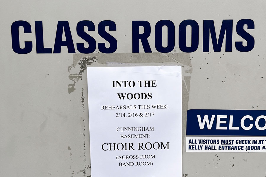 A sign outside the theater classrooms provides information about "In the Woods" rehearsals.