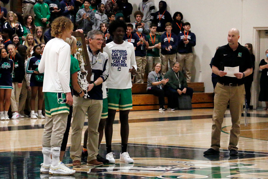 As Head Coach Mr. Jason Delaney looks on, members of the men's basketball team present the Class 4A State championship trophy to the school. 